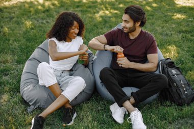 Indian boy and african girl talking sitting on the bean bag chairs in a park