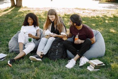Three friends with bottles of juice sitting on the bean bag chairs in a park
