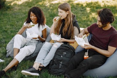 Three friends with bottles of juice sitting on the bean bag chairs in a park