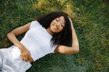 Female african student posing looking at camera lying on a grass in a park