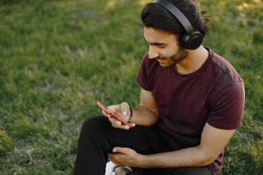 Male indian student sitting on a grass and using a smatphone