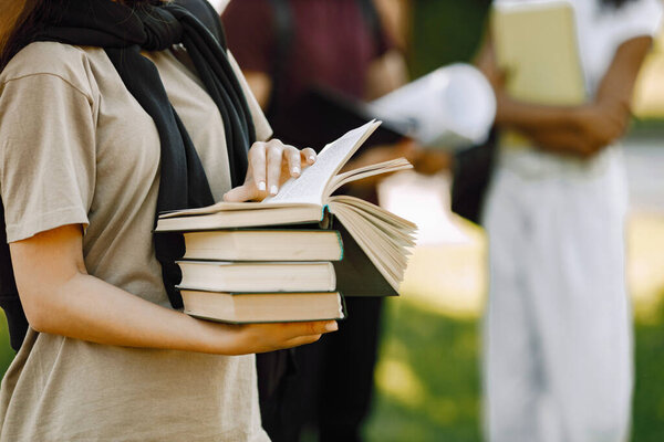 Three international students standing in a park and holding a books