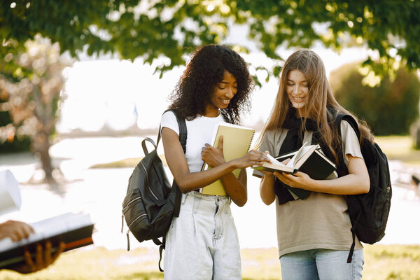 Two international students standing in a park and holding a books