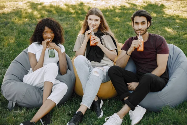 Three friends with bottles of juice sitting on the bean bag chairs in a park — Zdjęcie stockowe