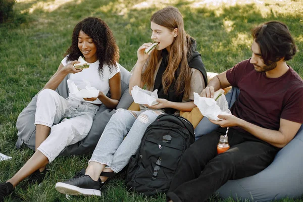 Three friends with bottles of juice sitting on the bean bag chairs in a park — Zdjęcie stockowe