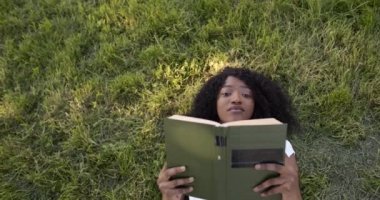 Woman reading while lying on grass alone