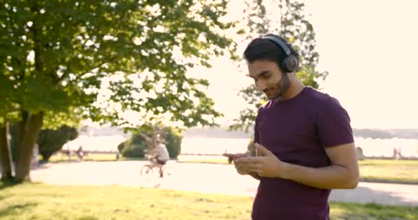 Pakistani young man listening to music in a green park — 비디오