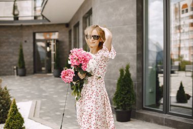 Young blonde woman standing near cafe and holding a bouquet of f