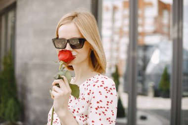 Young blonde woman standing near cafe and holding one rose