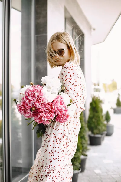Young blonde woman standing near cafe and holding a bouquet of flowers — Stock Photo, Image