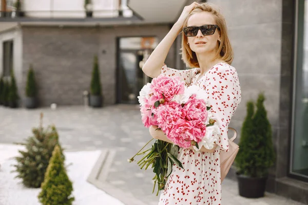 Young blonde woman standing near cafe and holding a bouquet of f