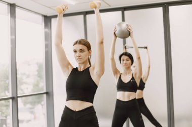 Three girls in a bright gym doing functional training with equipment