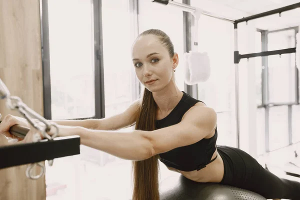 Young woman in a gym looking in a camera and stretching on a fitball — Fotografia de Stock