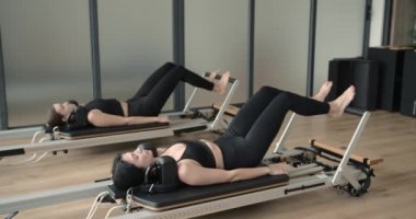Two women performing exercise on a reformer bed