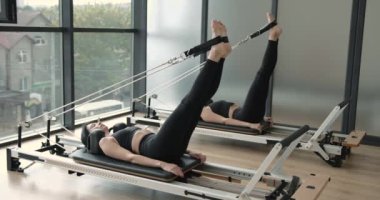 Two women performing exercise on a reformer bed