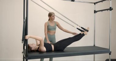 European woman doing pilates on reformer bed with coach