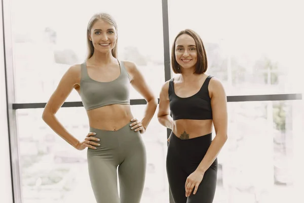 Blonde and brunette young women in a gym looking in a camera and smiling — стоковое фото