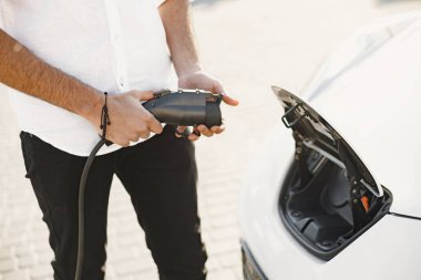 Young Arab man recharging white electric car