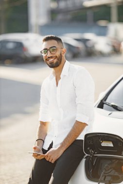 Young man use phone and drink coffee while charging car