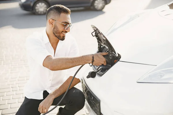 Young Arab man recharging white electric car — Foto Stock