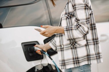 Elektrikli arabalardaki iş kadını telefon kullanarak şarj oluyor.