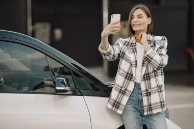 Arabasının yanında cep telefonu kullanan esmer bir kadının portresi.