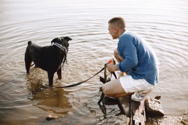 Man with rotweiller dog playing together in the lake