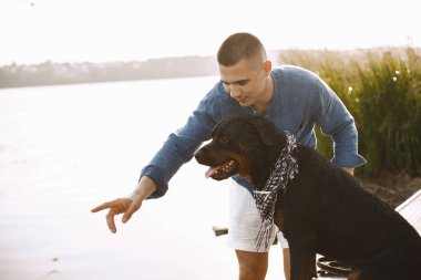 Man with rotweiller dog standing together near the lake