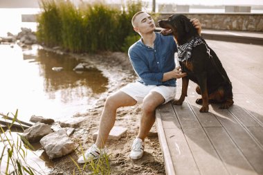 Man with rotweiller dog sitting together near the lake