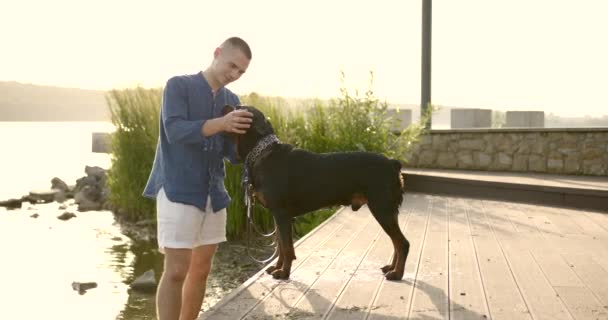 Молодий чоловік проводить час зі своїм собакою берег річки — стокове відео