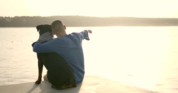 Man and dog sitting on the dock at a lake — Stok video