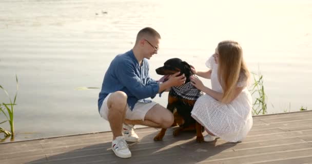 Loving young couple with a dog by lake — 图库视频影像