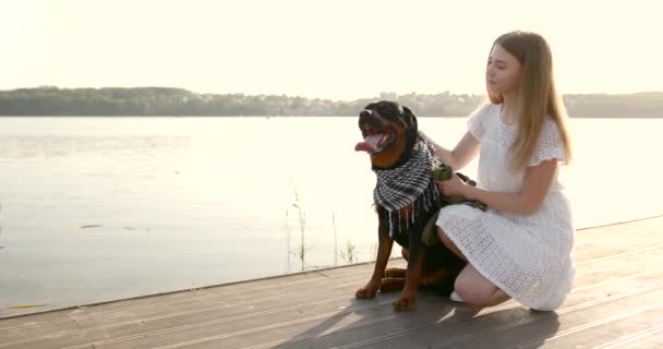 Young woman stroking black rottweiler on lake pier — kuvapankkivideo