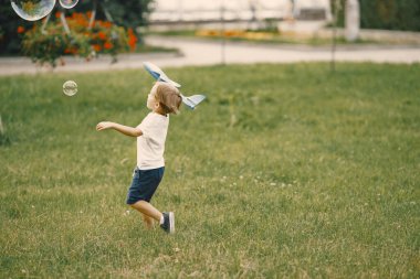 Küçük çocuk çimlerin üzerinde uçak oyuncağıyla oynuyor.