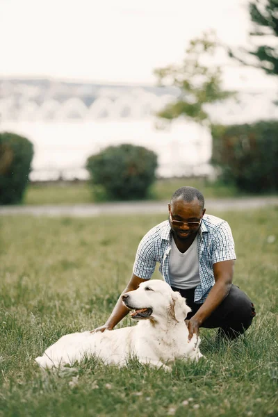 Negro americano hombre en un gafas de sol sentado con tiene perro en un hierba — Foto de Stock
