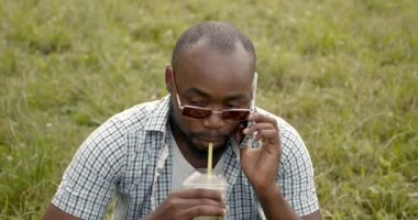 Neşeli yakışıklı siyah erkek çimlerin üzerinde oturuyor.