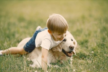 Küçük çocuk çimlerin üzerinde köpeğiyle oynuyor.