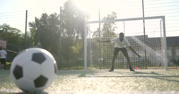 Primer plano de la pelota en el campo mientras el hombre de pie en la red de fútbol — Vídeos de Stock