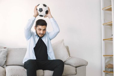 Esmer adam koçta oturuyor ve evde maç izliyor.