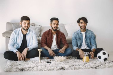 Üç Hintli adam yerde oturup TV 'de futbol izliyorlar.
