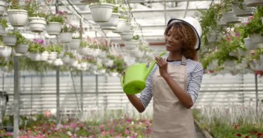 Yeşil evde çiçekleri sulayan gülümseyen kadın.