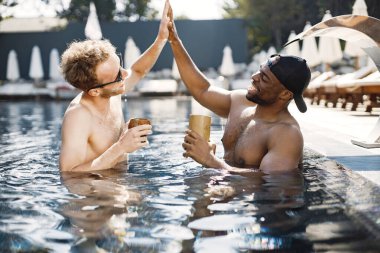 İki erkek arkadaş yüzme havuzunda kokteyl içerek rahatlıyor.