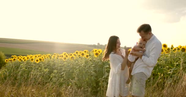 Молода сім'я з маленьким сином добре проводять час на соняшниковому полі на заході сонця — стокове відео
