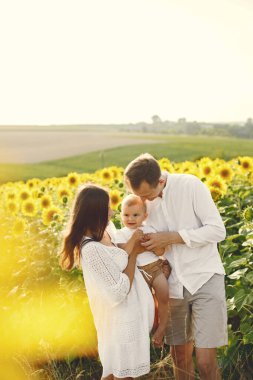 Anne, baba ve oğul ayçiçeği tarlasında beyaz elbiseli.