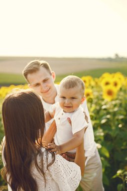 Anne, baba ve oğul ayçiçeği tarlasında beyaz elbiseli.