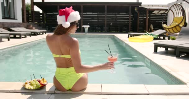 圣诞节的女人在游泳池边放松 有趣的女孩庆祝圣诞节在一个度假胜地 配上鸡尾酒和水果 — 图库视频影像