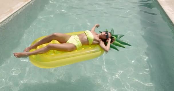 年轻女子在游泳池日光浴中漂浮在菠萝气垫上 — 图库视频影像