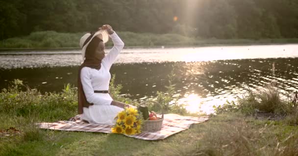Femme noire dans le chapeau assis sur la couverture à la rivière — Video