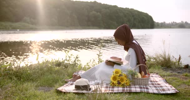 Donna nera in abito bianco lettura presso la riva del fiume — Video Stock