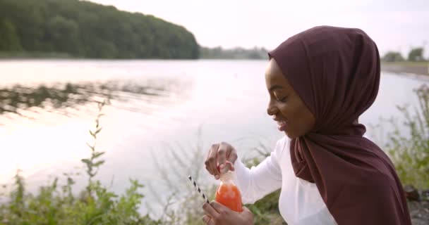 Donna nera musulmana che beve coktail alla riva del fiume — Video Stock